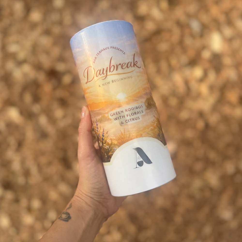 Hand holding a cylindrical product labeled 'Daybreak' against a blurred natural background